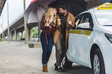 Birbirimizi taksi yakın dururken gülümseyen şemsiye ile mutlu genç çift