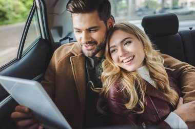 Genç çift birlikte arabada otururken dijital tablet kullanarak gülümseyen