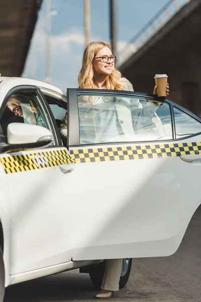 コーヒーに行くとタクシーのドアを開けるしながら探している Cab を保持している眼鏡で幸せなブロンドの女の子 — ストック写真