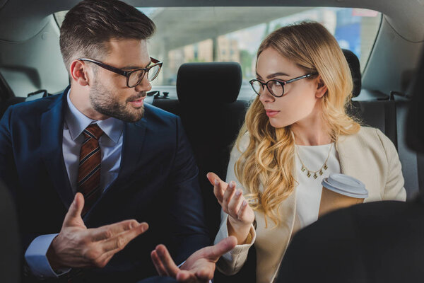 young man and woman in formal wear and eyeglasses talking while sitting together in car