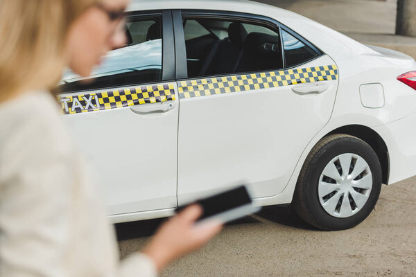 selective focus young woman using smartphone while standing near taxi cab