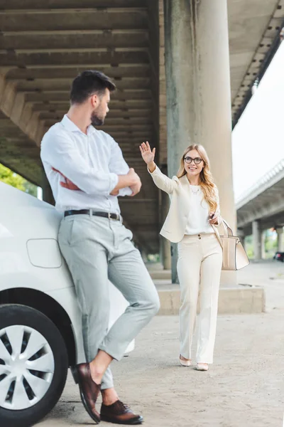 Lachende Jonge Vrouw Brillen Hand Zwaaien Naar Man Leunend Auto — Gratis stockfoto