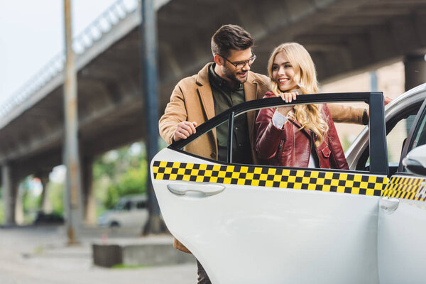 happy stylish young couple opening door of taxi cab together