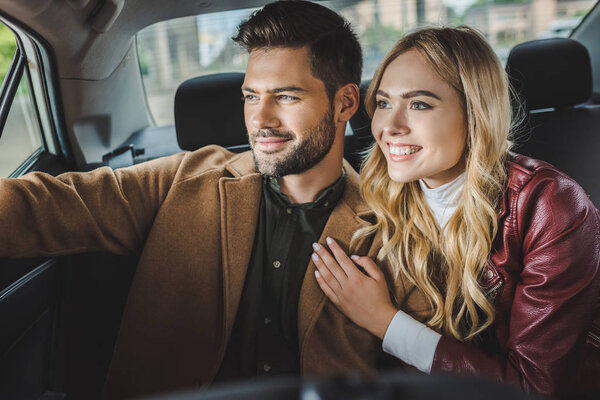 улыбающаяся молодая пара смотрит в окно машины, сидя вместе в такси

