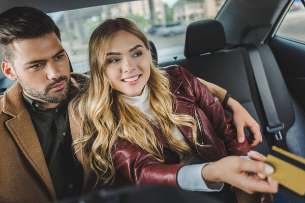 stylish young couple sitting together in taxi, girl holding credit card