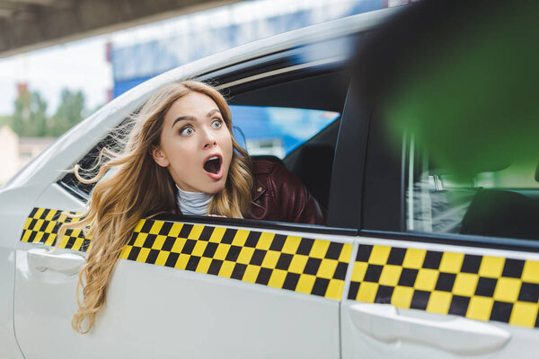 selective focus of shocked girl looking away through taxi window 