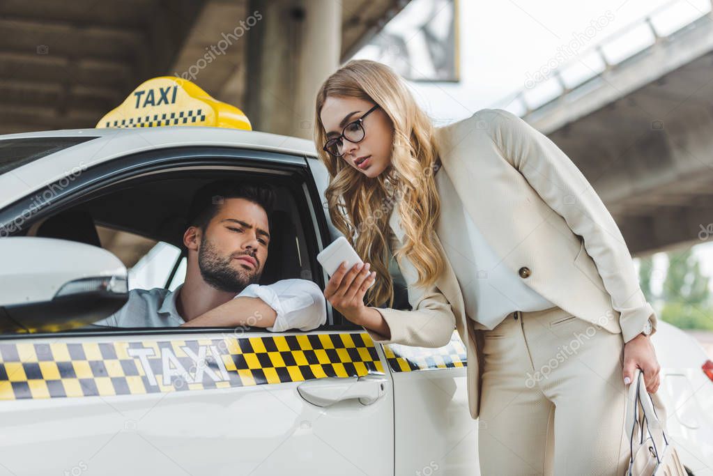 stylish blonde woman showing smartphone to the taxi driver