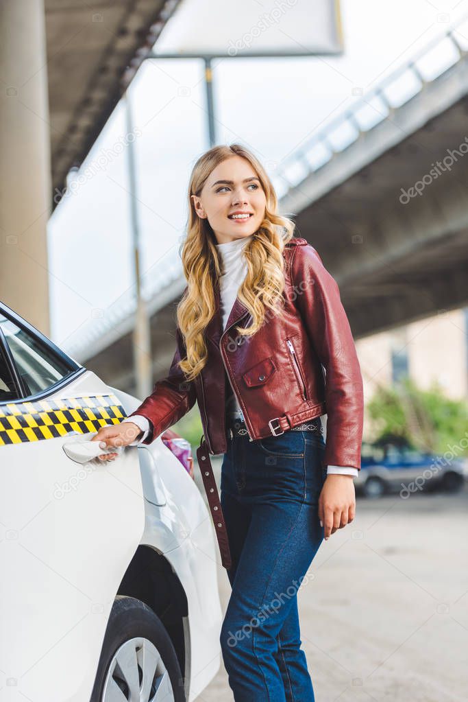 happy young woman opening door of taxi and looking away 