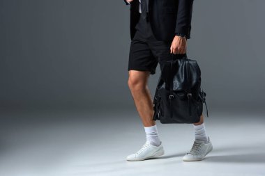 cropped image of stylish man in shorts holding backpack on grey background  clipart