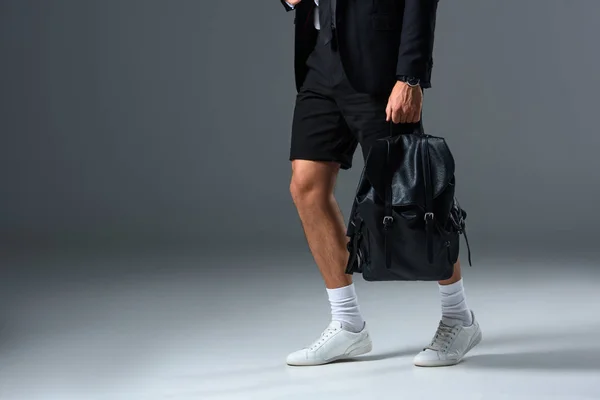 灰色の背景にバックパックを保持のショート パンツでスタイリッシュな男の画像をトリミング — ストック写真