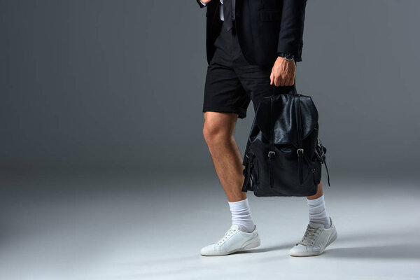 cropped image of stylish man in shorts holding backpack on grey background 