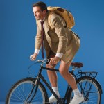 Focused man with backpack riding bicycle and looking away on blue