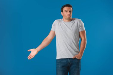 surprised man gesturing with hand and looking at camera isolated on blue clipart