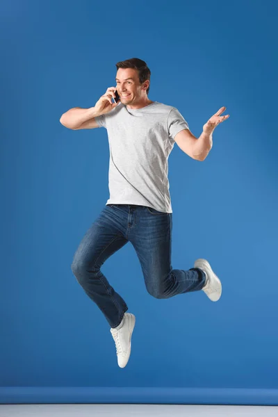 Hombre Feliz Hablando Por Teléfono Inteligente Saltando Azul —  Fotos de Stock