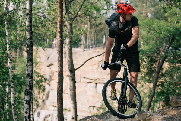 young male extreme cyclist in protective helmet riding on mountain bicycle in forest