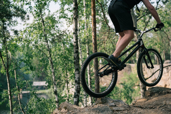 cropped image of male extreme cyclist jumping on mountain bike in forest