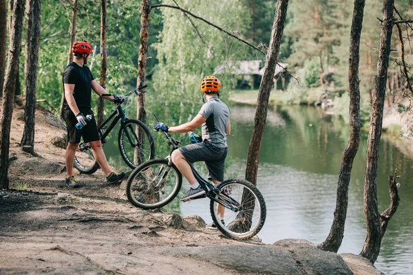 水のスポーツ ボトルと休憩と森林の川を見て マウンテン バイクのヘルメットで男性の極端な自転車の背面図  — 無料ストックフォト