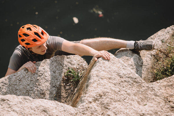 high angle view of focused male hiker in protective helmet climbing on rocks 