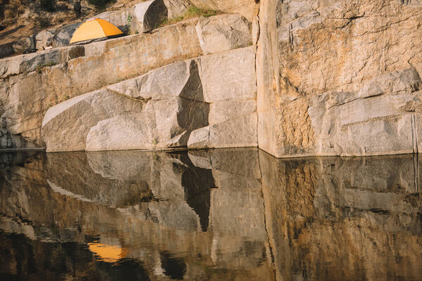 distant view of travel tent on rocky cliff over river 