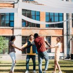 Multikulturní mladí přátelé drží za ruce zároveň baví společně v letním dni