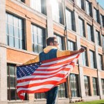 Back view of young man with american flag in hands on street