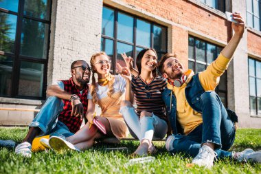 çok ırklı arkadaşlar selfie smartphone üzerinde yeşil çimenlerin üzerine birlikte dinlenme süre alarak gülümseyen