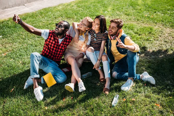 Amigos Multiétnicos Tomando Selfie Teléfono Inteligente Mientras Descansan Césped Verde — Foto de stock gratis