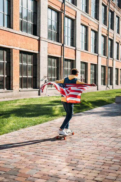Вид сзади человека с флагом США, катающегося на лонгборде на улице
