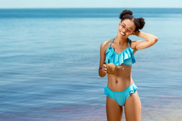 Sonriente Mujer Afroamericana Bikini Sosteniendo Cóctel Concha Coco Frente Mar — Foto de stock gratis