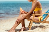 levágott kép nő alkalmazása fényvédő krém a bőr homokos strandon nyugágy ülve 