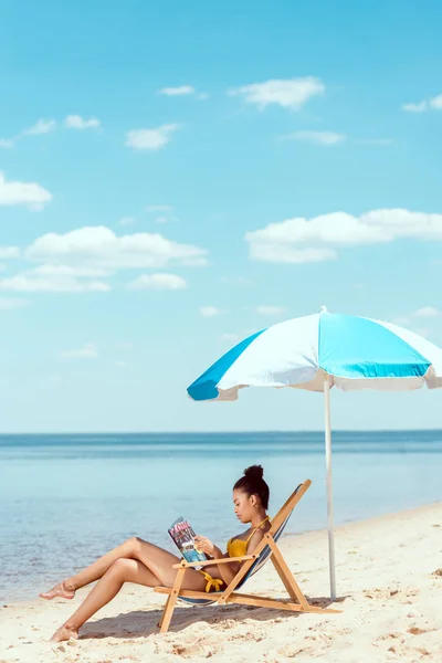 Vista Lateral Joven Mujer Afroamericana Leyendo Revista Relajarse Tumbona Bajo — Foto de Stock