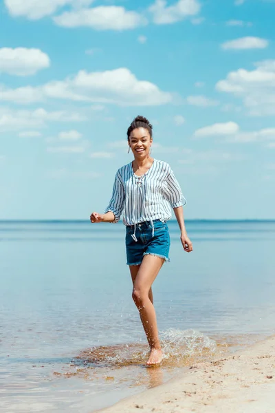 Smilende Afroamerikansk Kvinne Som Løper Sjøvann Nær Sandstranden – stockfoto