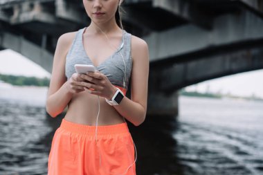 Genç sporcumuz earphones ve smartwatch ile smartphone kullanarak görünümünü kırpılmış