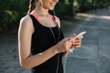 sporcumuz kulaklık ile müzik dinleme gülümseyen ve smartphone kullanarak kırpılmış görünümü