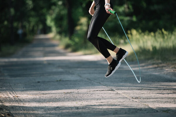 cropped view of sportswoman jumping on skipping rope in park
