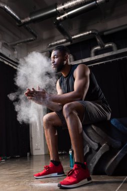 Lastik içinde oturan ve talk pudrası ellerde uygulayarak Afrika kökenli Amerikalı sporcu düşük açılı görünümü