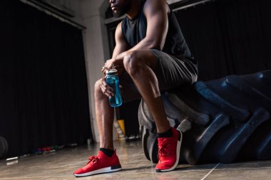 lastiği ve su şişe tutan spor salonunda oturan genç Afro-Amerikan sporcu kırpılmış atış