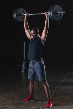 full length view of muscular african american sportsman lifting barbell in gym clipart