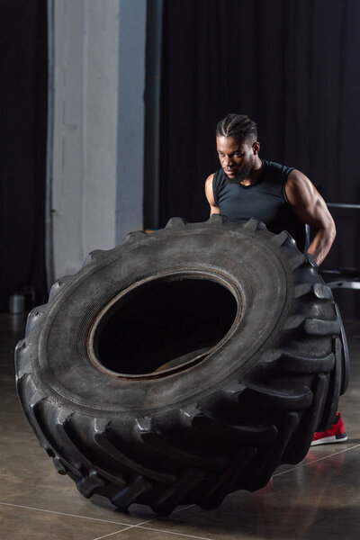 handsome muscular young african american sportsman training with tire