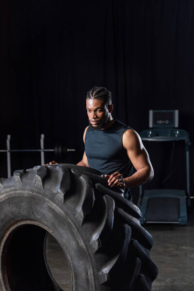 serious muscular african american sportsman exercising with tyre