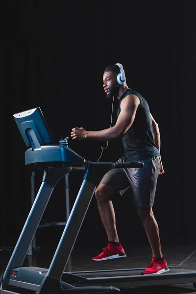 英俊的年轻非洲裔美国运动员在跑步机上运行耳机的侧面视图 — 图库照片
