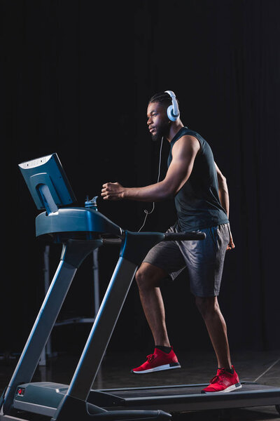 side view of handsome young african american sportsman in headphones running on treadmill