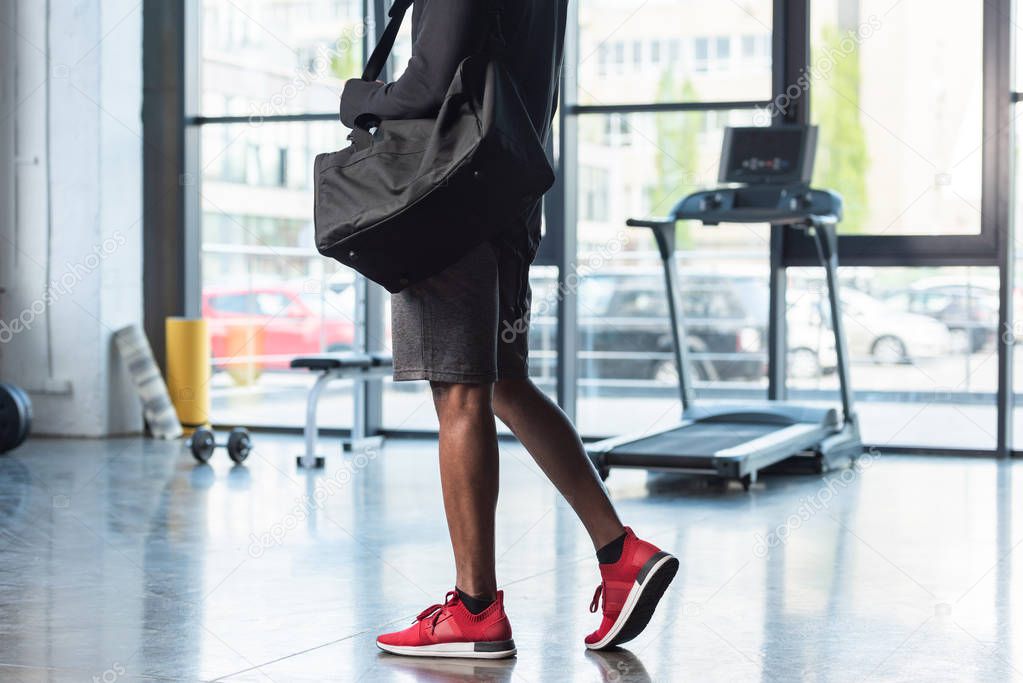 cropped shot of african american man in sportswear holding bag in gym