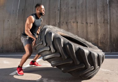 side view of concentrated african american sportsman training with tire on street