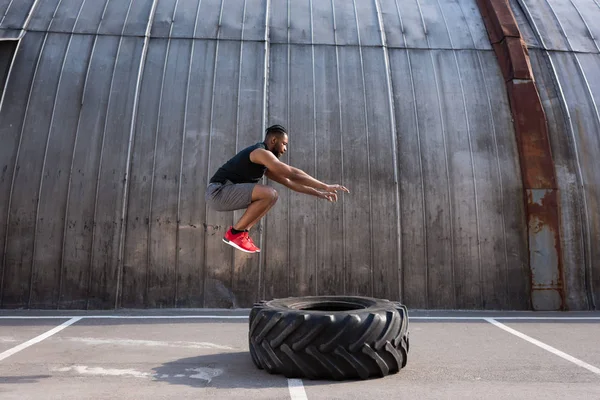 Musculoso Deportista Afroamericano Saltando Mientras Entrena Con Neumático Calle — Foto de Stock