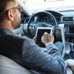 Partial view of businessman in eyeglasses using tablet in car