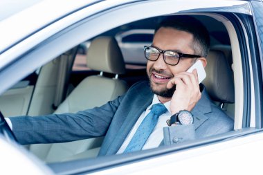 Smartphone'da araba sürüş sırasında konuşurken gülümseyen iş adamı 
