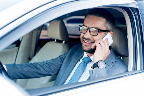 smiling businessman talking on smartphone while driving car 