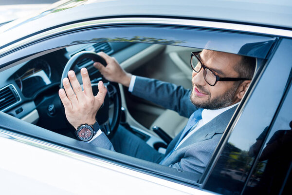 smiling businessman in suit and eyeglasses greeting someone while driving car