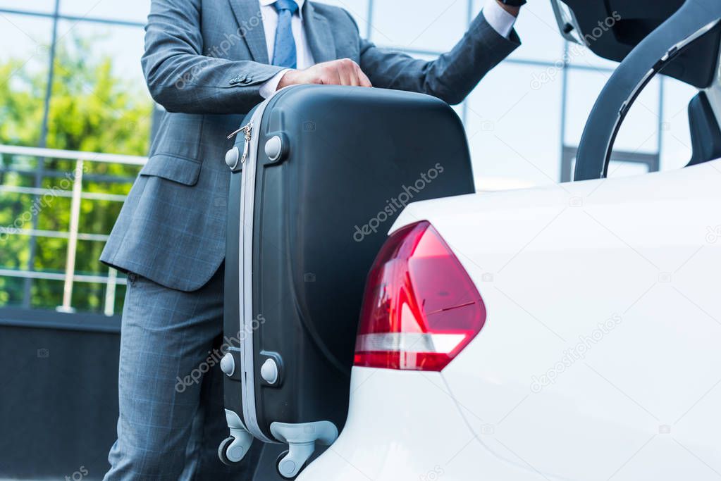 partial view of businessman putting luggage into car on parking